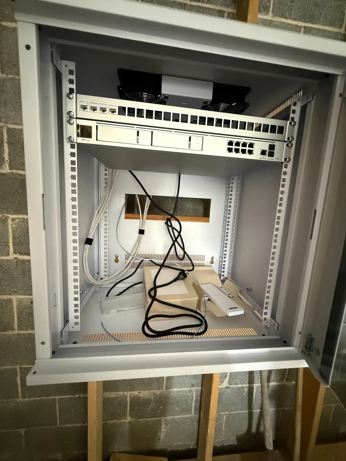 Interior of a wall-mount communications cabinet with network equipment staged for installation